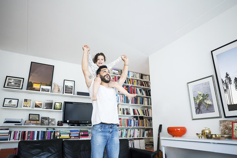 Low angle view of man carrying daughter on shoulder while standing in living room at home Photograph by Maskot