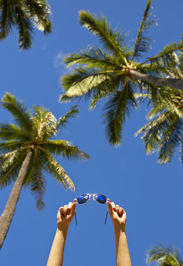 Low angle view of Pacific Islander woman holding sunglasses under palm trees Photograph by Colin Anderson Productions pty ltd