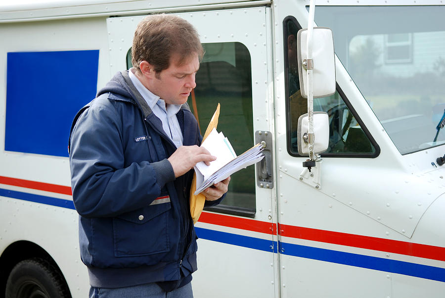 Mail carrier sorting mail near delivery truck Photograph by BassittART