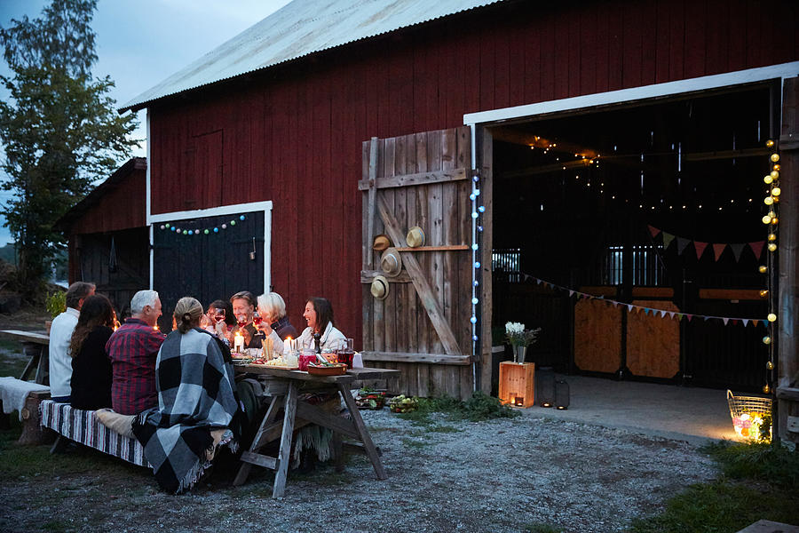 Male and female friends enjoying dinner party against barn at farm Photograph by Maskot