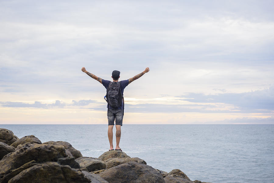 Male backpacker standing on rocks with arms outstretched Photograph by JohnnyGreig
