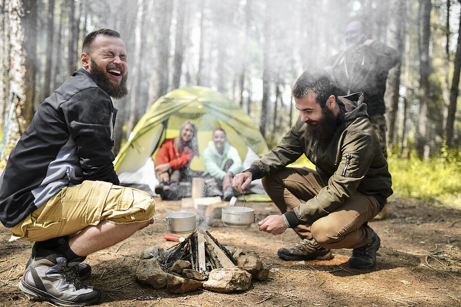 Male Camper Closing Eyes From Smoke While Lighting Fire In Forest Camp With Friends Photograph by AleksandarGeorgiev