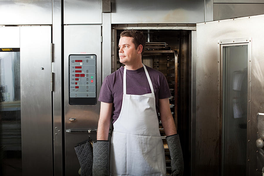 Male chef standing in front of oven Photograph by Image Source