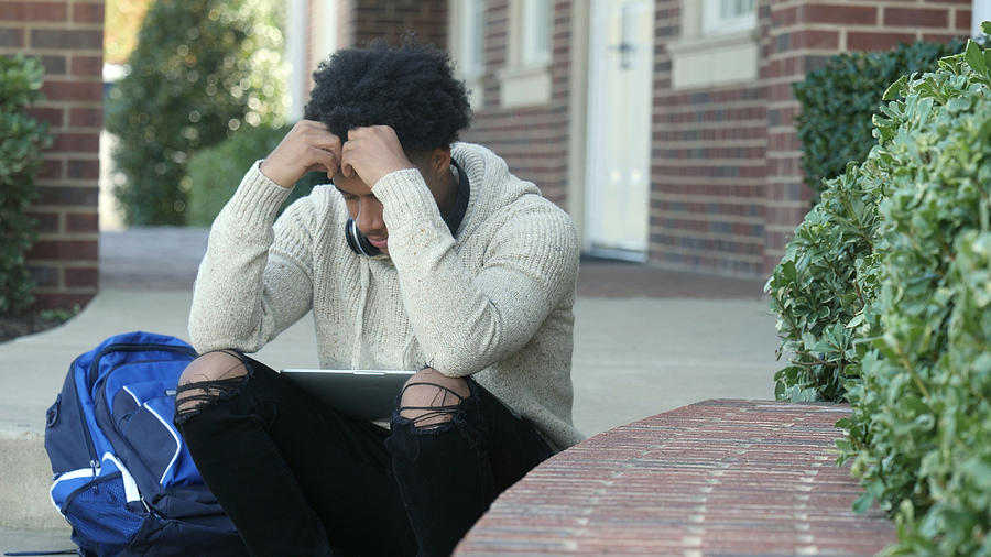 Male college student rests head in hands while sitting on staircase Photograph by SDI Productions