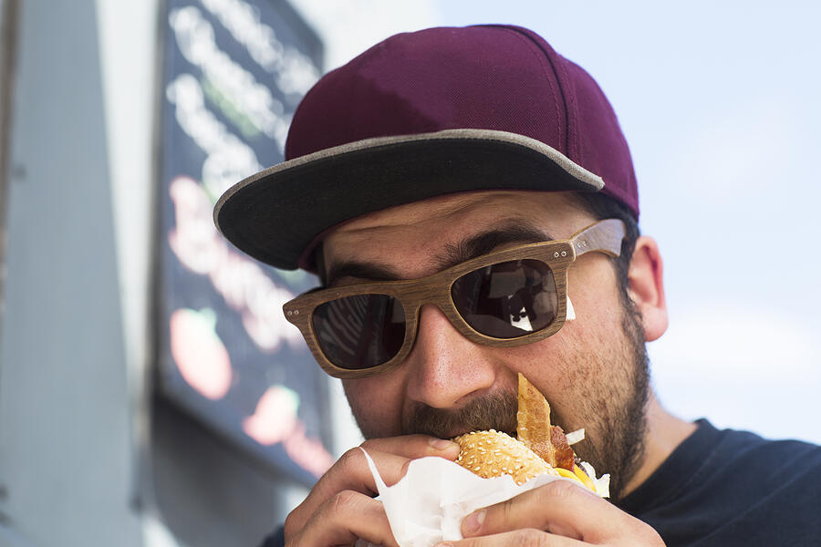 Male customer eating hamburger from fast food van Photograph by Sigrid Gombert