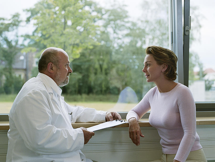 Male doctor sitting with female patient by window, side view Photograph by Jochen Sands