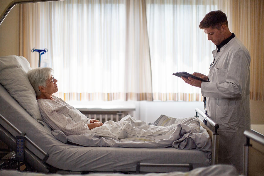 Male doctor visiting senior patient in hospital ward Photograph by Luis Alvarez Male doctor visiting senior patient in hospital ward Photograph by Luis Alvarez