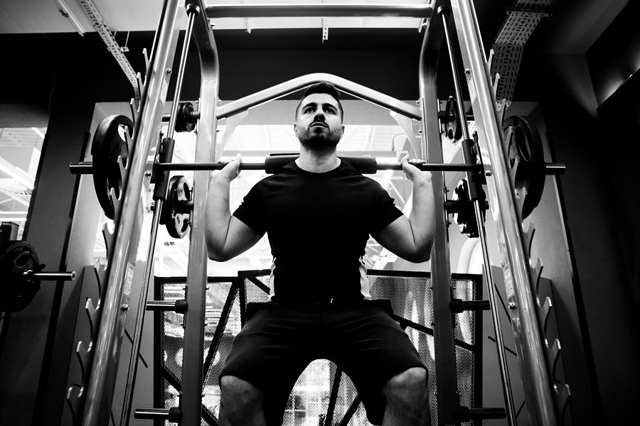 Male fitness athlete in the gym performing squats on Smith machine Photograph by Photographer, Basak Gurbuz Derman