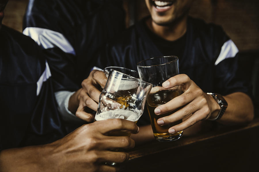 Male football fans toasting beer glasses in bar Photograph by The Good Brigade