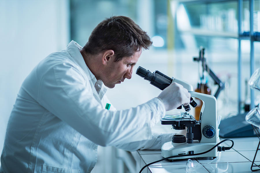 Male forensic scientist examining something through a microscope. Photograph by BraunS