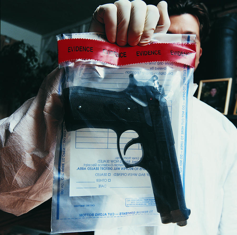 Male Forensic Scientist Holding an Evidence Bag With a Gun Inside Photograph by Digital Vision.