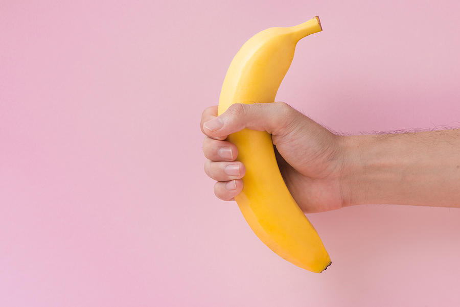 Male hand holding a banana isolated on pink background. Photograph by Makidotvn