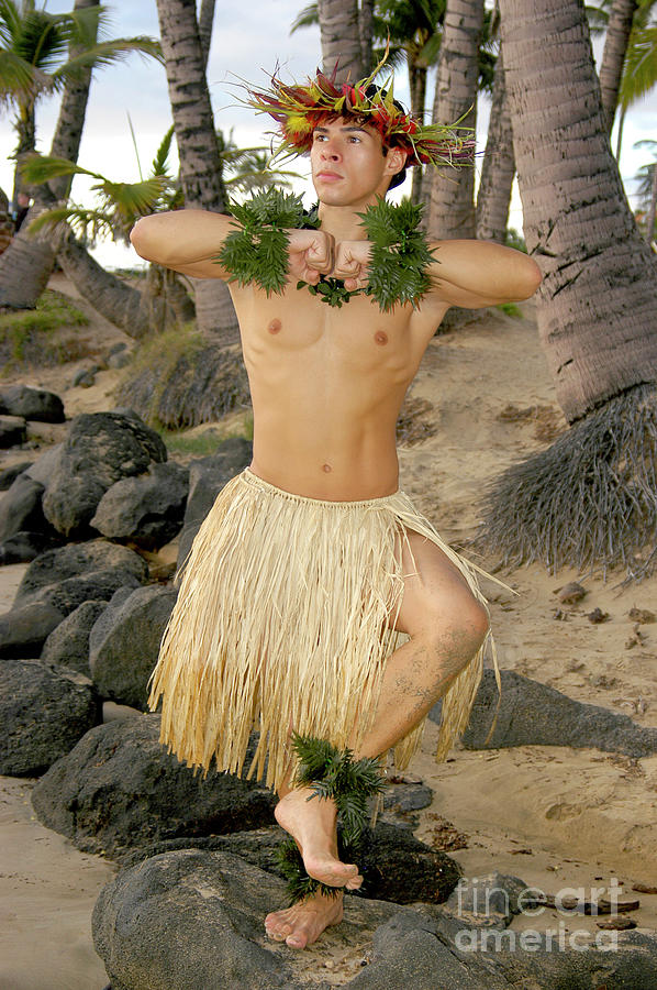 Male hula dancer poses in front of palm trees on the beach.	 Photograph by Gunther Allen