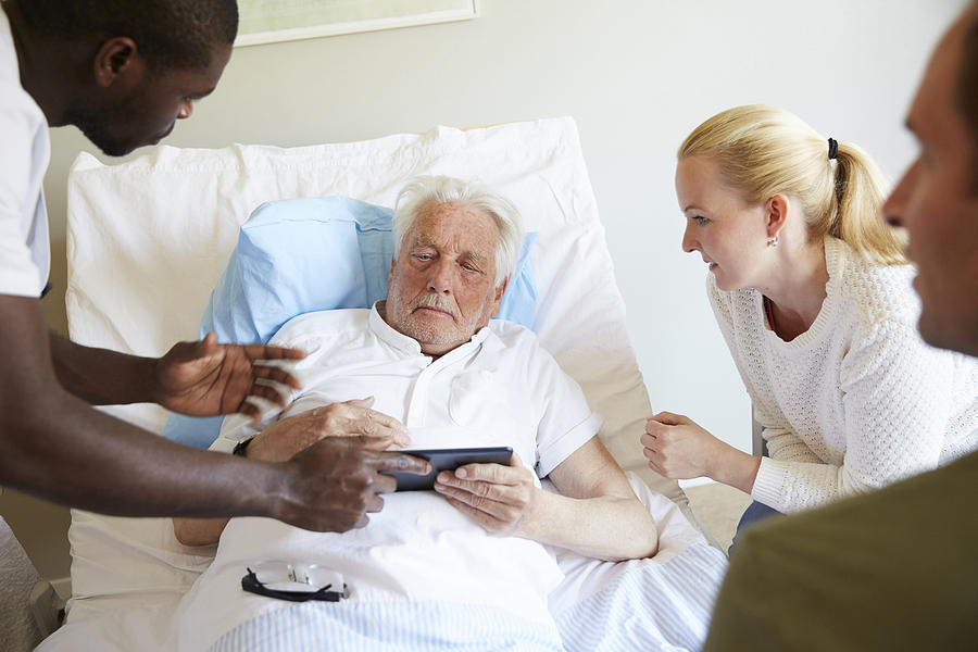 Male nurse showing digital tablet to senior man and couple at hospital ward Photograph by Maskot