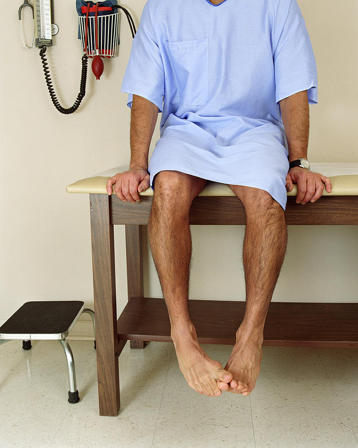 Male patient sitting on examining room table, mid section Photograph by PM Images