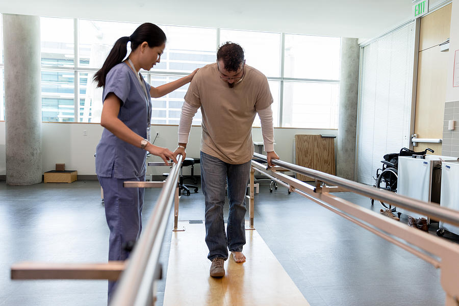 Male patient takes first steps using orthopedic parallel bars Photograph by SDI Productions