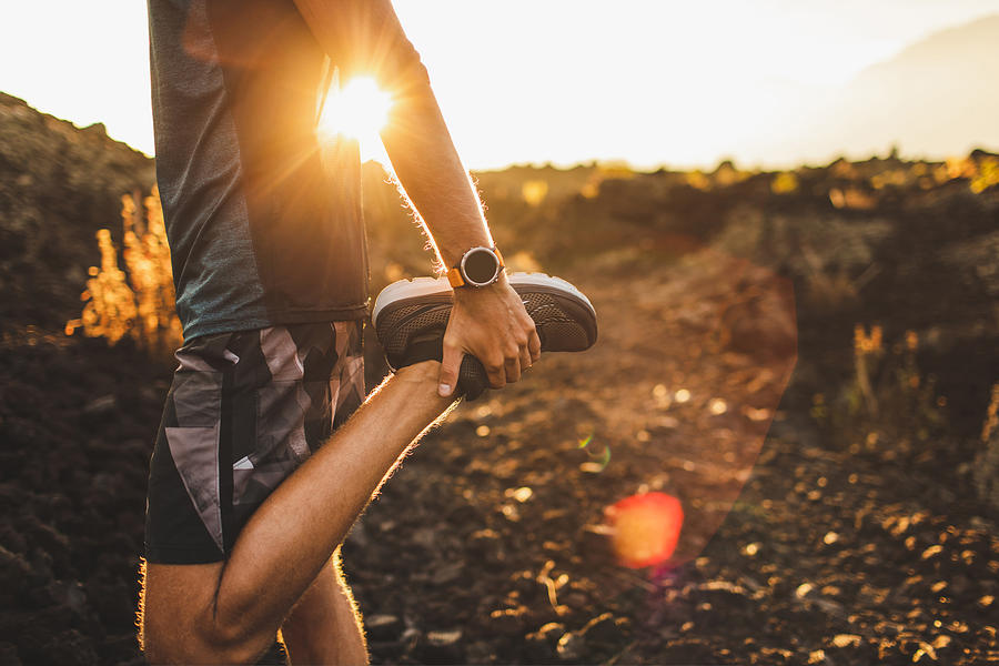 Male runner stretching leg and feet and preparing for running outdoors. Smart watch or fitness tracker on hand. Beautiful sun light on background. Active and healthy lifestyle concept. Photograph by Olegbreslavtsev