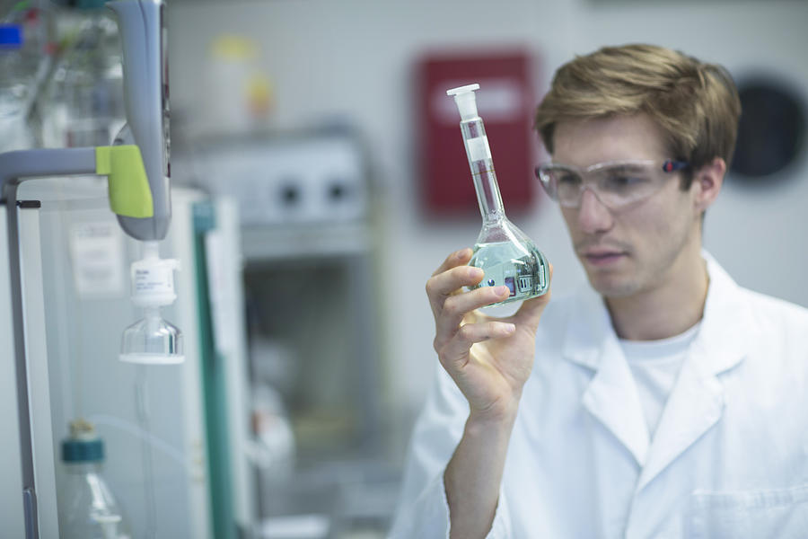 Male scientist looking at flask in lab Photograph by Sigrid Gombert