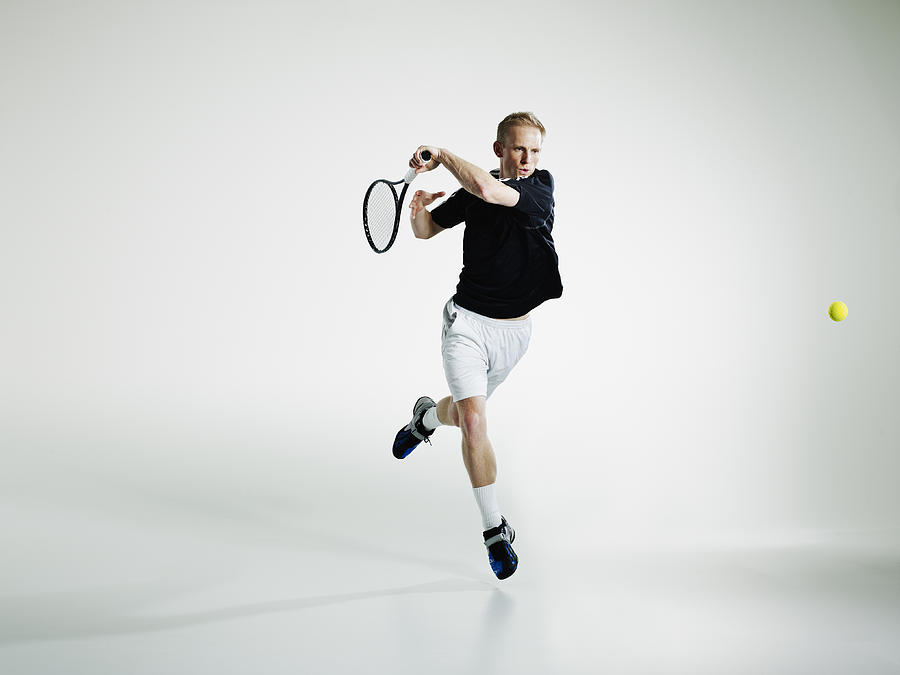 Male tennis player in mid air returning ball Photograph by Thomas Barwick