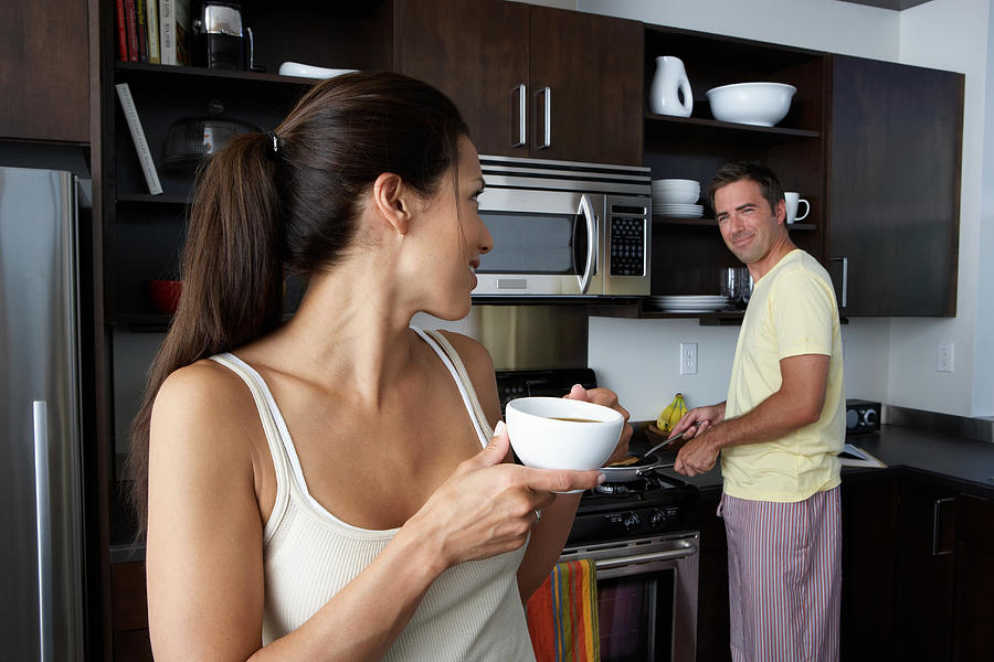 Man and woman preparing breakfast and smiling at one another Photograph by Thomas Northcut