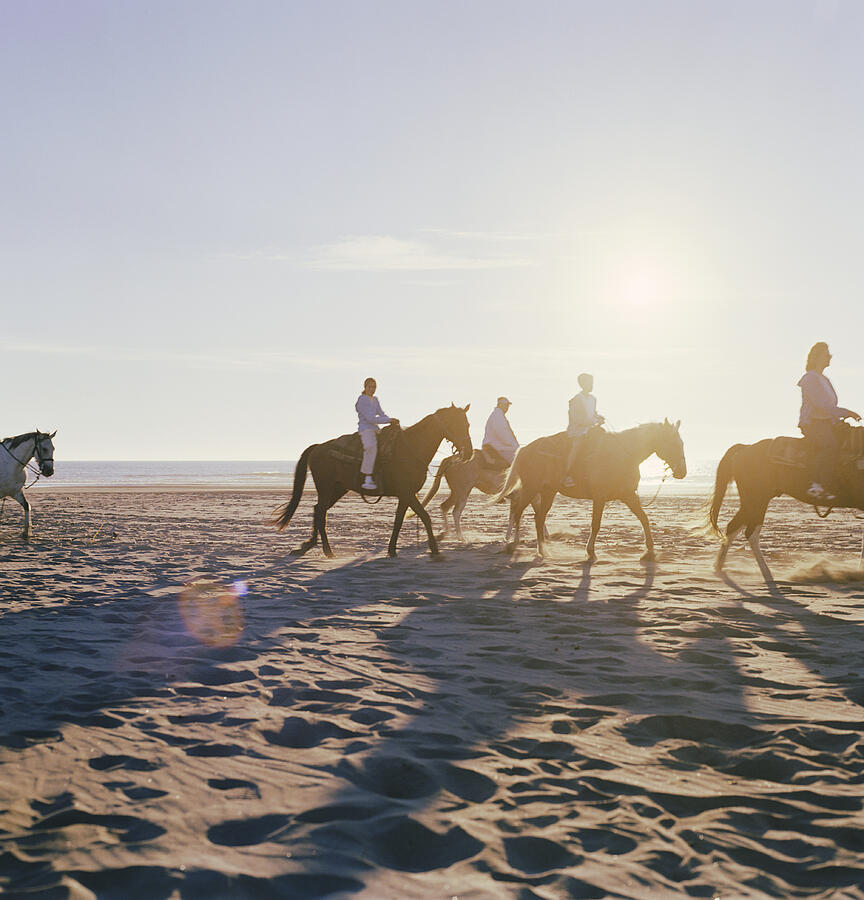 Man and woman riding horses on beach with children (7-11), side view Photograph by Ryan McVay