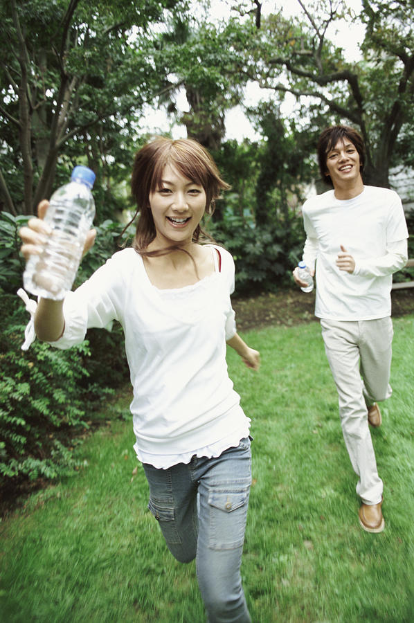 Man and Woman Running Outdoors, Woman Holding a Water Bottle Photograph by Digital Vision.