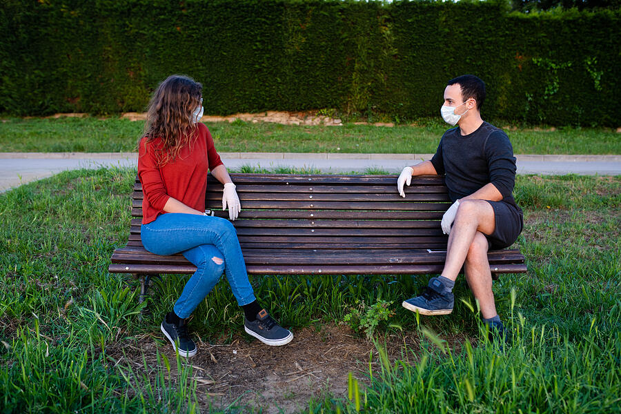 man and woman sitting on a bench in the park, keeping social distance wearing mask and gloves. Covid lifestyle Photograph by Alex Cambero 