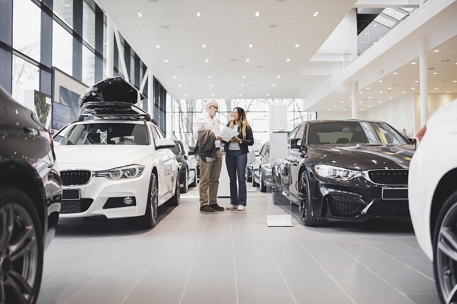 Man and woman with paper standing amidst cars at showroom Photograph by Maskot