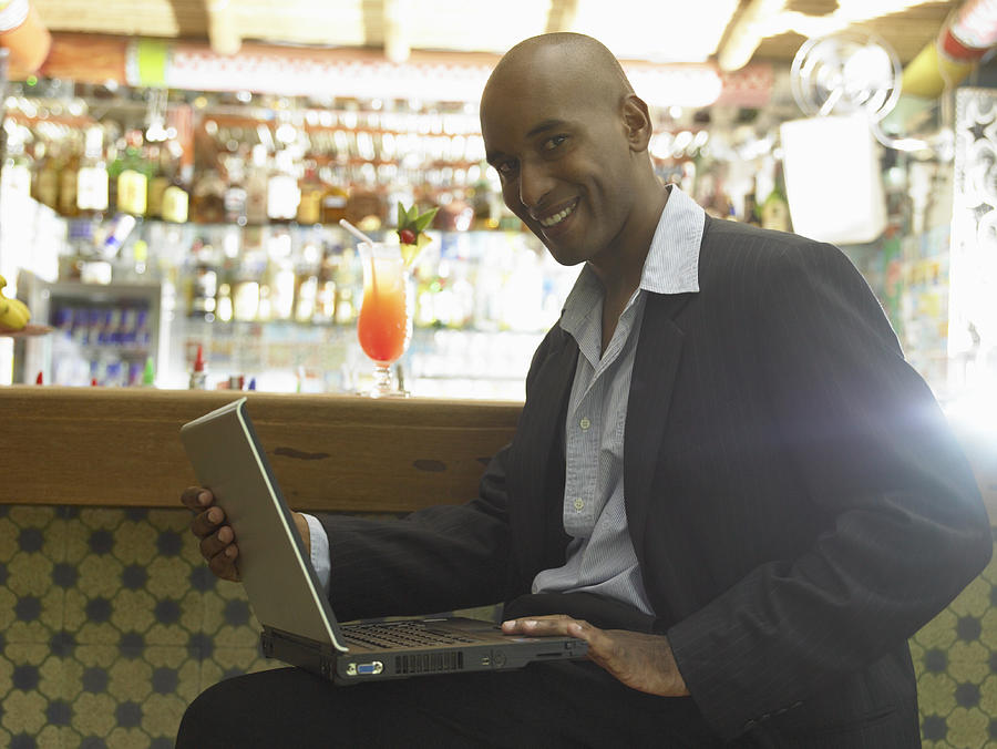 Man at bar with laptop, smiling, portrait Photograph by Hans Neleman