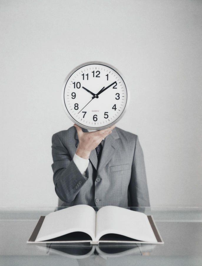 Man at table in suit holding clock in front of head, open book on table Photograph by PhotoAlto/Matthieu Spohn