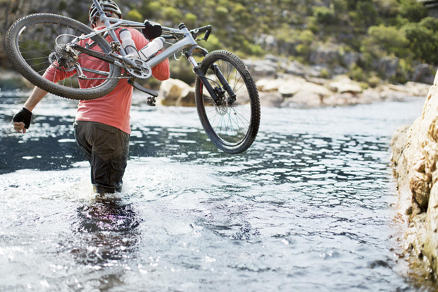 Man carrying mountain bike in river Photograph by Caia Image