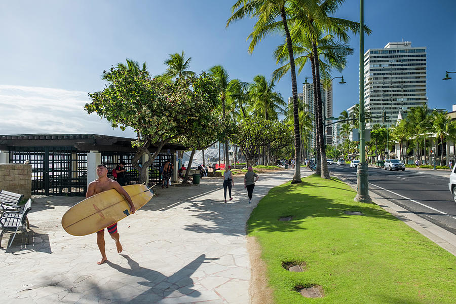 Man carrying surfboard walking on the sidewalk along Kalakaua Av Photograph by David L Moore