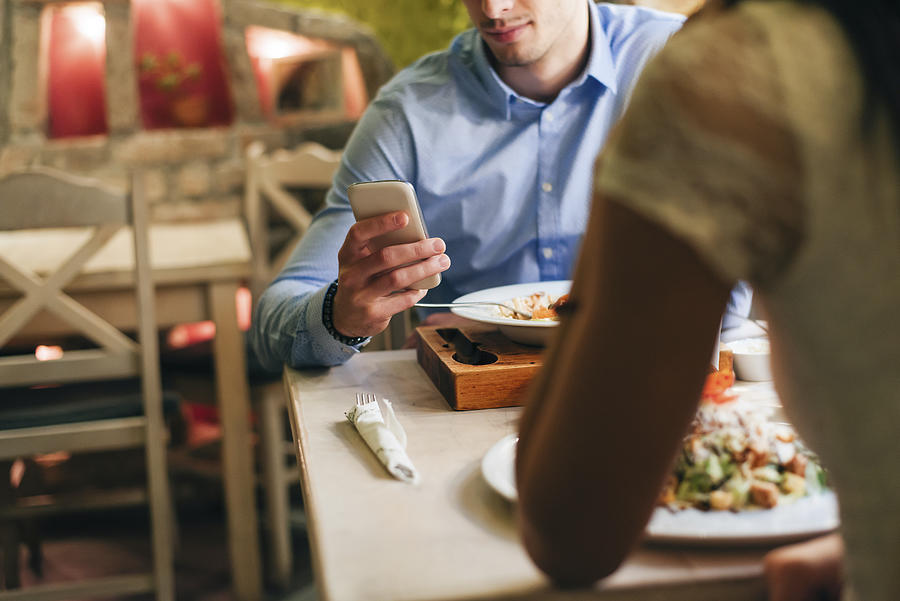 Man checking messages while having dinner in a restaurant Photograph by Westend61