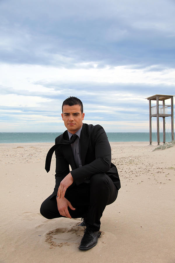 Man crouching on beach Photograph by Sergi Albir / Archerphoto