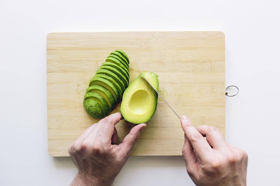 Man cutting avocado on a wooden cutting board, personal perspective directly above view Photograph by Alexander Spatari