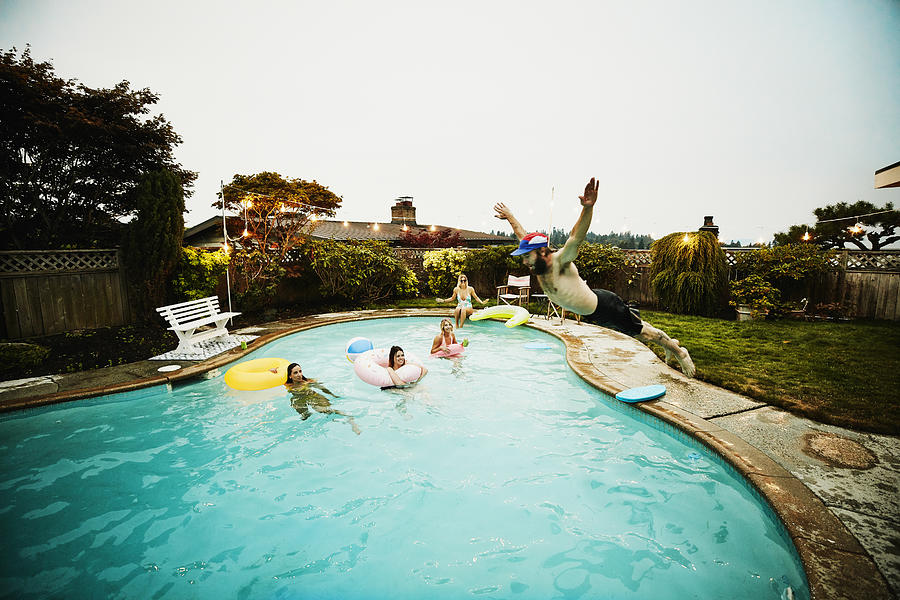 Man doing belly flop into backyard pool during party with friends on summer evening Photograph by Thomas Barwick