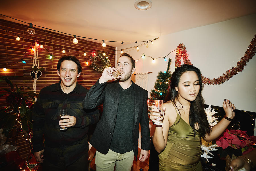 Man drinking champagne while hanging out with friends during holiday party Photograph by Thomas Barwick