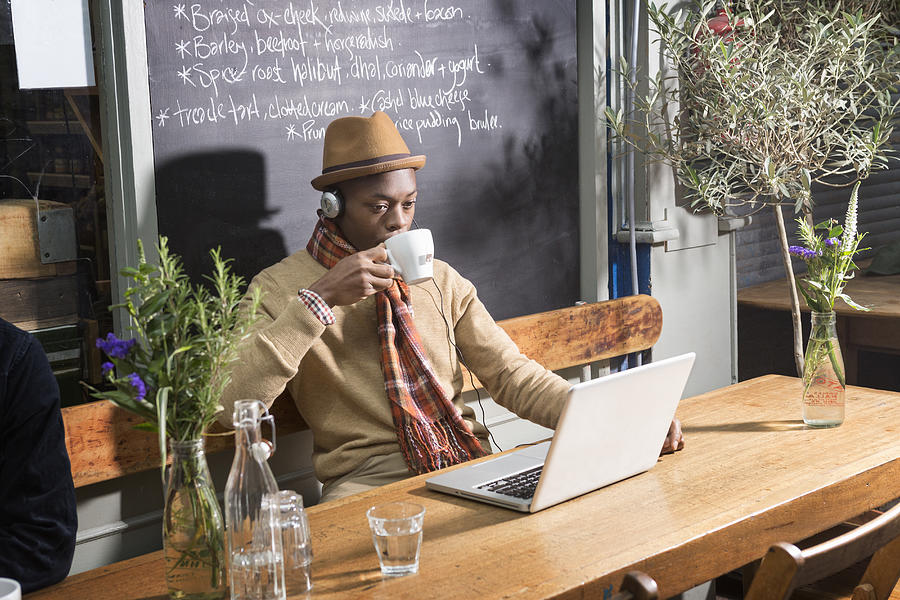 Man drinking tea while at laptop in urban cafe. Photograph by Betsie Van Der Meer