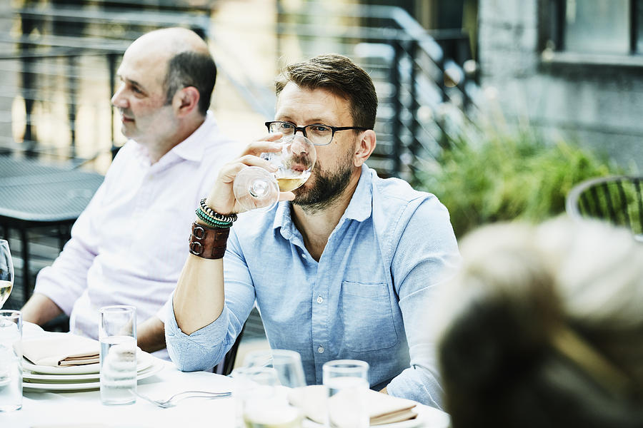 Man drinking wine while sharing dinner with friends on restaurant patio Photograph by Thomas Barwick