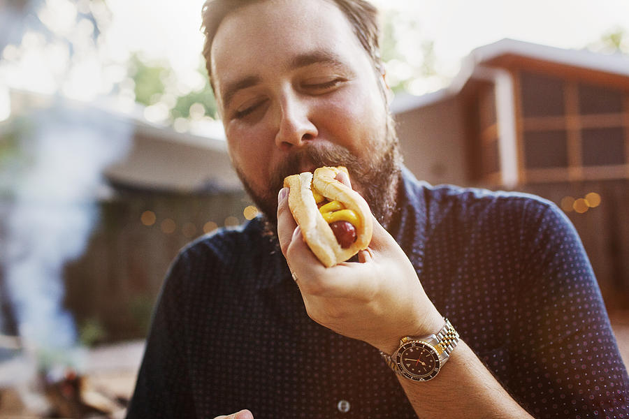 Man eating hot dog at yard Photograph by Cavan Images