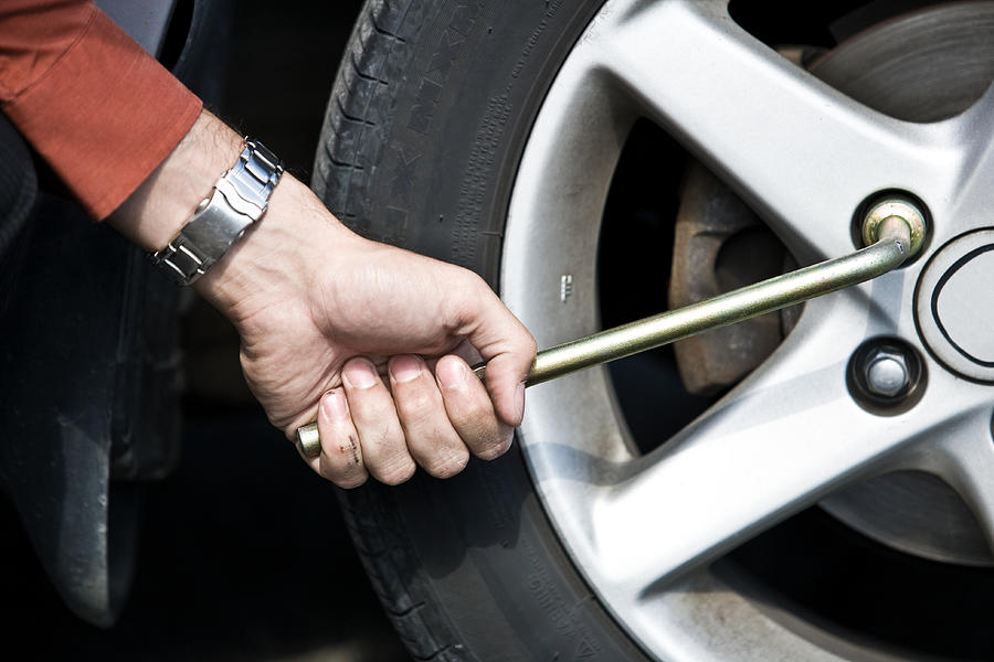 Man gripping tire iron and loosening lug nuts Photograph by Jupiterimages