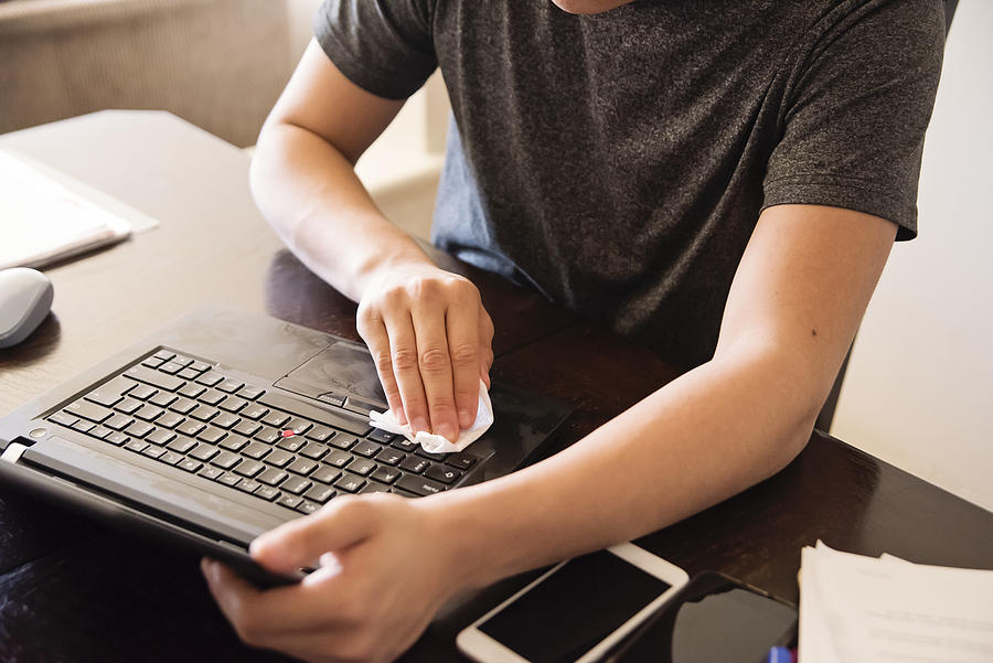 Man hands wiping laptop while working from home. Photograph by Martinedoucet
