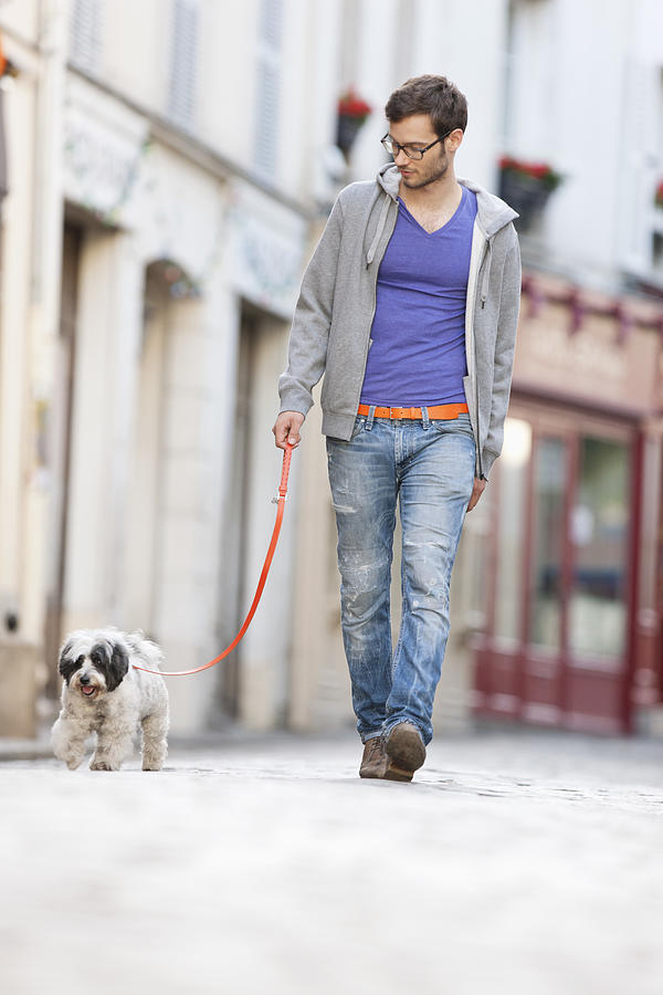 Man holding a dog on leash walking on the street, Paris, Ile-de-France, France Photograph by Fabrice LEROUGE