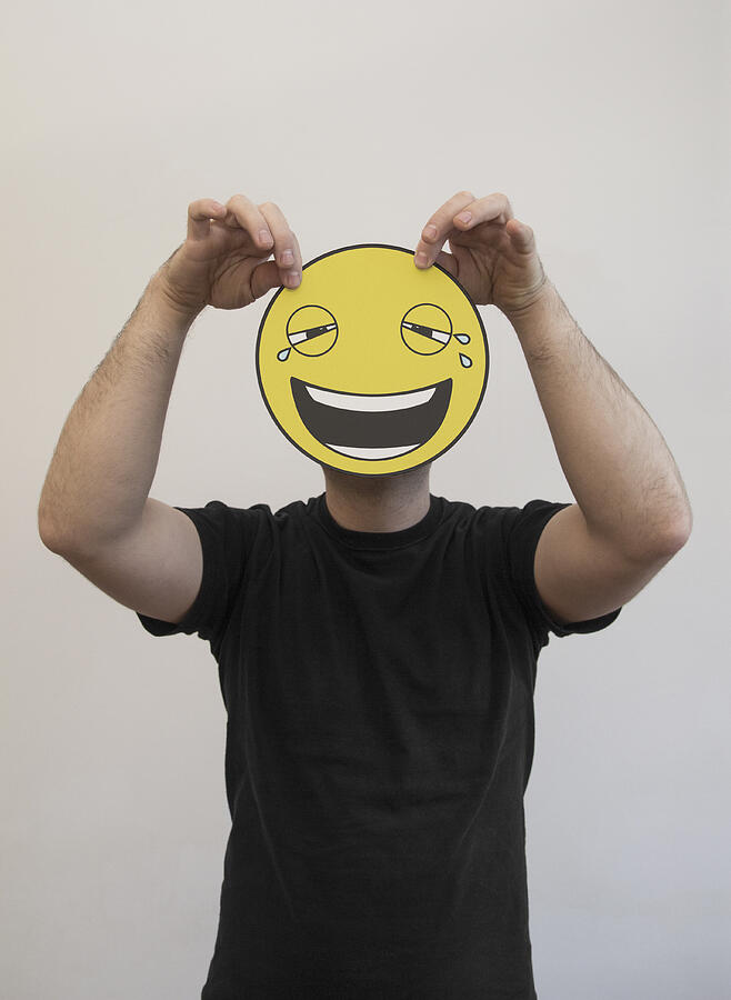 Man holding a laughing and crying emoticon face in front of his face Photograph by Malte Mueller