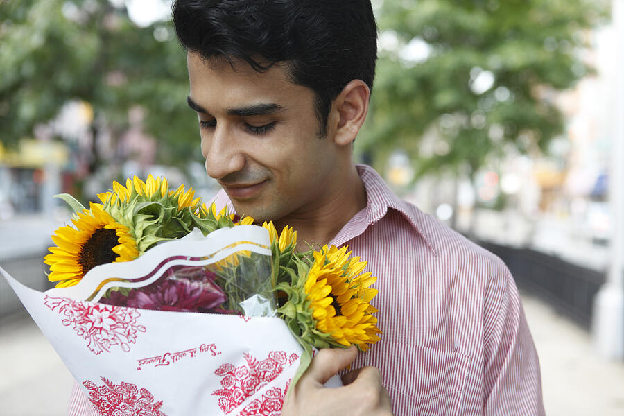 Man holding bouquet of flowers in city, smiling Photograph by Tim Kitchen