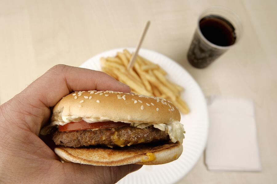 Man holding burger above french fries and cup of cola Photograph by Martin Hospach