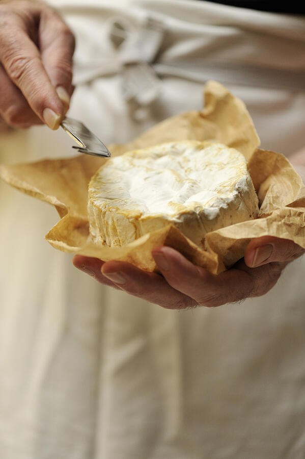 Man holding goats cheese and cheese knife, focus on hands Photograph by Diana Miller