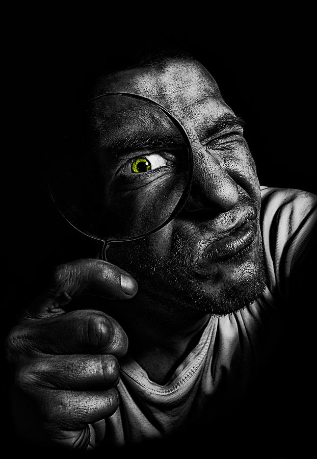 Man holding magnifying glass in front of his green colored eye. Investigating like a detective, looking into camera. Photograph by Photo by Jeff Krol