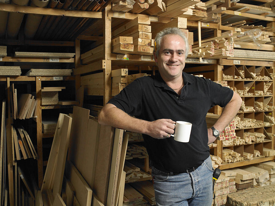 Man holding mug by planks of wood on shelves, smiling, portrait Photograph by Michael Blann