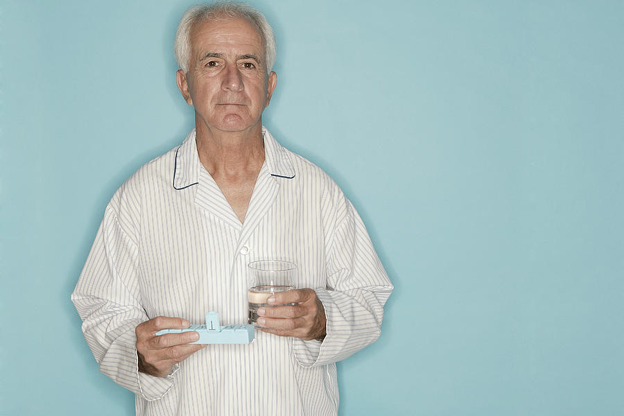 Man holding pill case and glass of water Photograph by Comstock Images